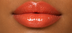 JJ Luxe Cosmetics Heatwave Peptide Lip Glaze on deep tan complexion lips in a glossy sheer coral finish.