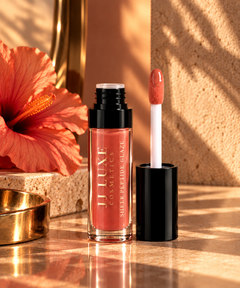 JJ Luxe Cosmetics Heatwave Sheer Peptide Glaze open tube and doe-foot applicator in glossy coral with hibiscus, warm stone and golden-hour styling