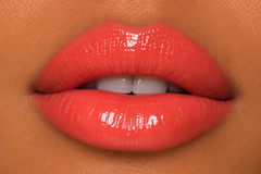 JJ Luxe Cosmetics Heatwave Sheer Peptide Glaze on tan complexion lips in a glossy sheer coral shade