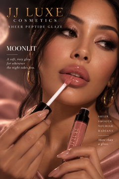 Model applying JJ Luxe Cosmetics Moonlit Sheer Peptide Glaze, a sheer blush-pink glossy lip color, in a warm rose moonlit editorial setting.