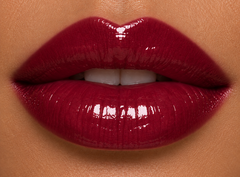 Tan complexion lips wearing JJ Luxe Cosmetics Nocturne Sheer Peptide Glaze in a glossy deep burgundy wine-plum shade.